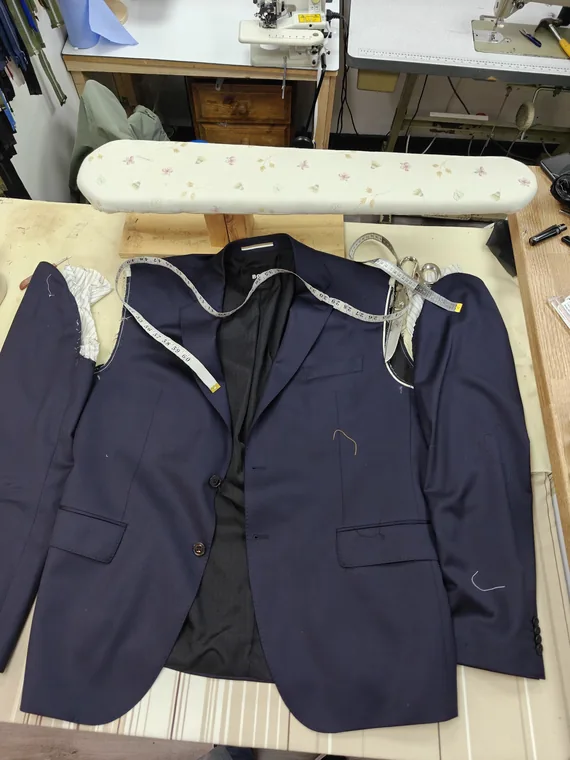 A navy suit jacket opened up on the pressing table mid-alteration