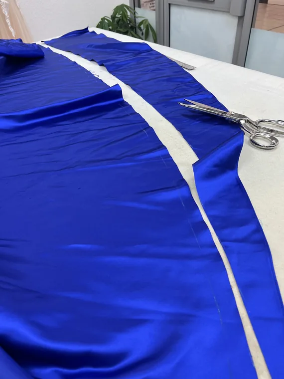 Royal blue satin being cut on the table with shears and a ruler