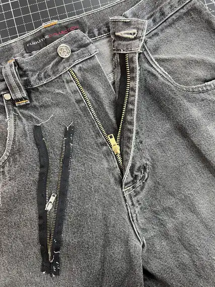 A worn zip cut out of a pair of grey jeans with replacement zips laid alongside